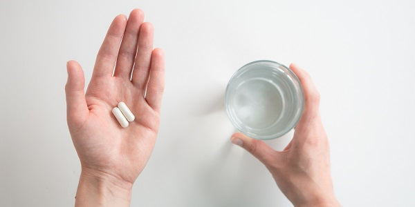 Prise de deux gélules de L-carnitine avec un verre d'eau