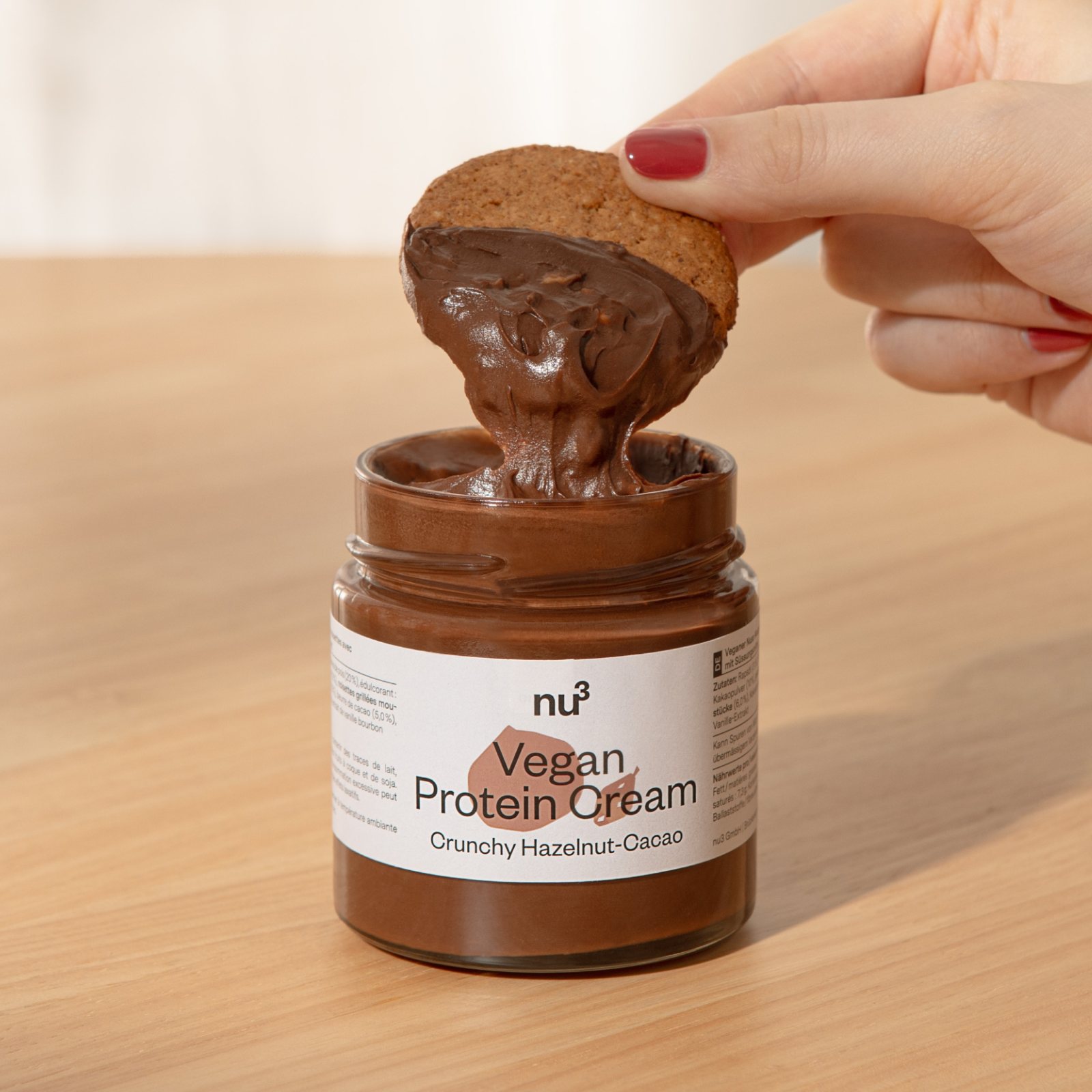 Main trempant un biscuit dans un verre contenant de la crème protéinée vegan nu3
