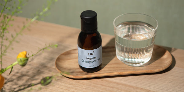 Huile oméga-3 vegan nu3 avec un verre d'eau
