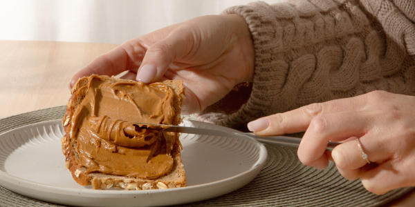 Main qui tartine une tranche de pain avec du beurre de cacahuètes