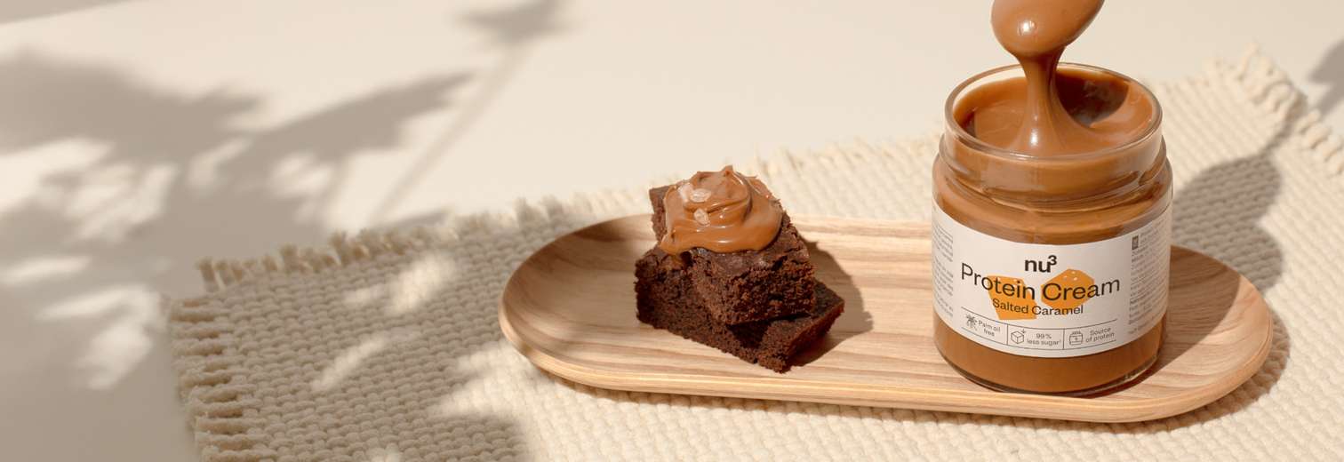 nu3 Protein Cream Salted Caramel sur une petite planche en bois, accompagné d'un brownie