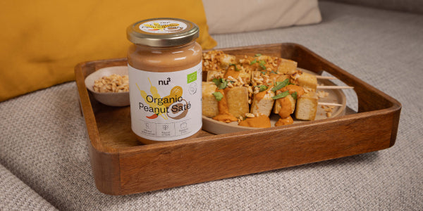 Verre avec sauce saté aux cacahuètes et brochettes de tofu sur un plateau